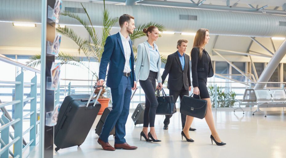 Business people walking briskly through an airport terminal, carrying briefcases and wearing professional attire.