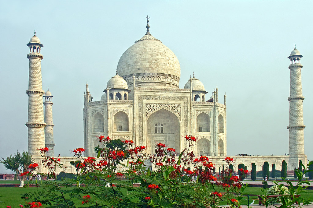 a white building with a dome and flowers with Taj Mahal in the background
