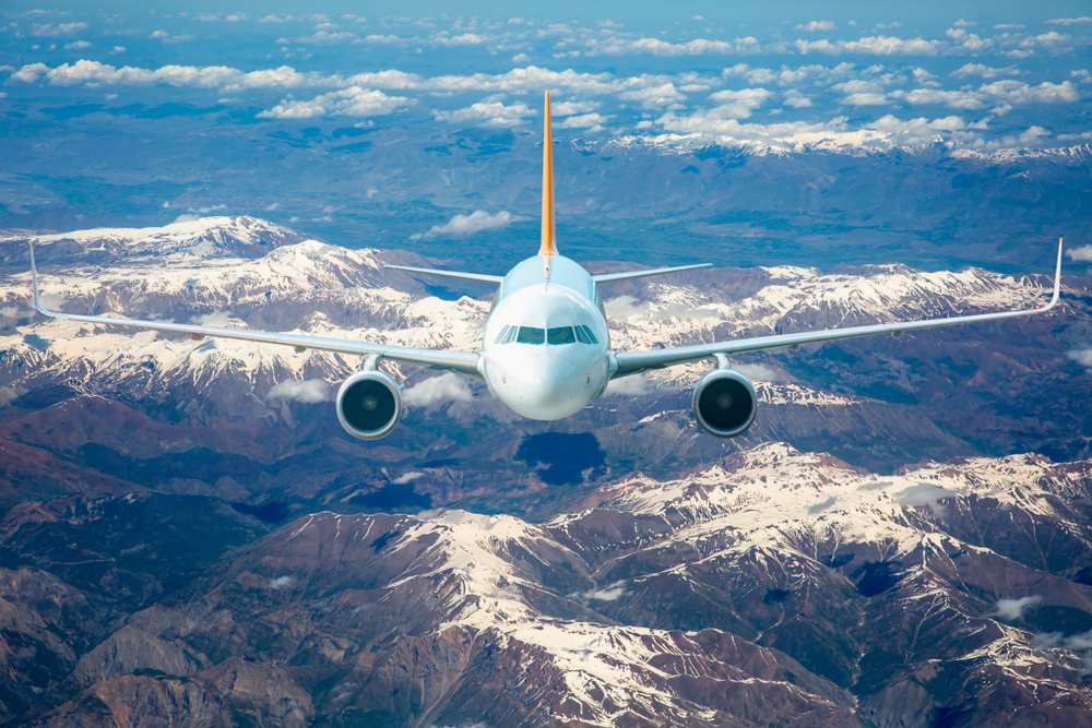 A large passenger jet soaring above snow-capped mountains.